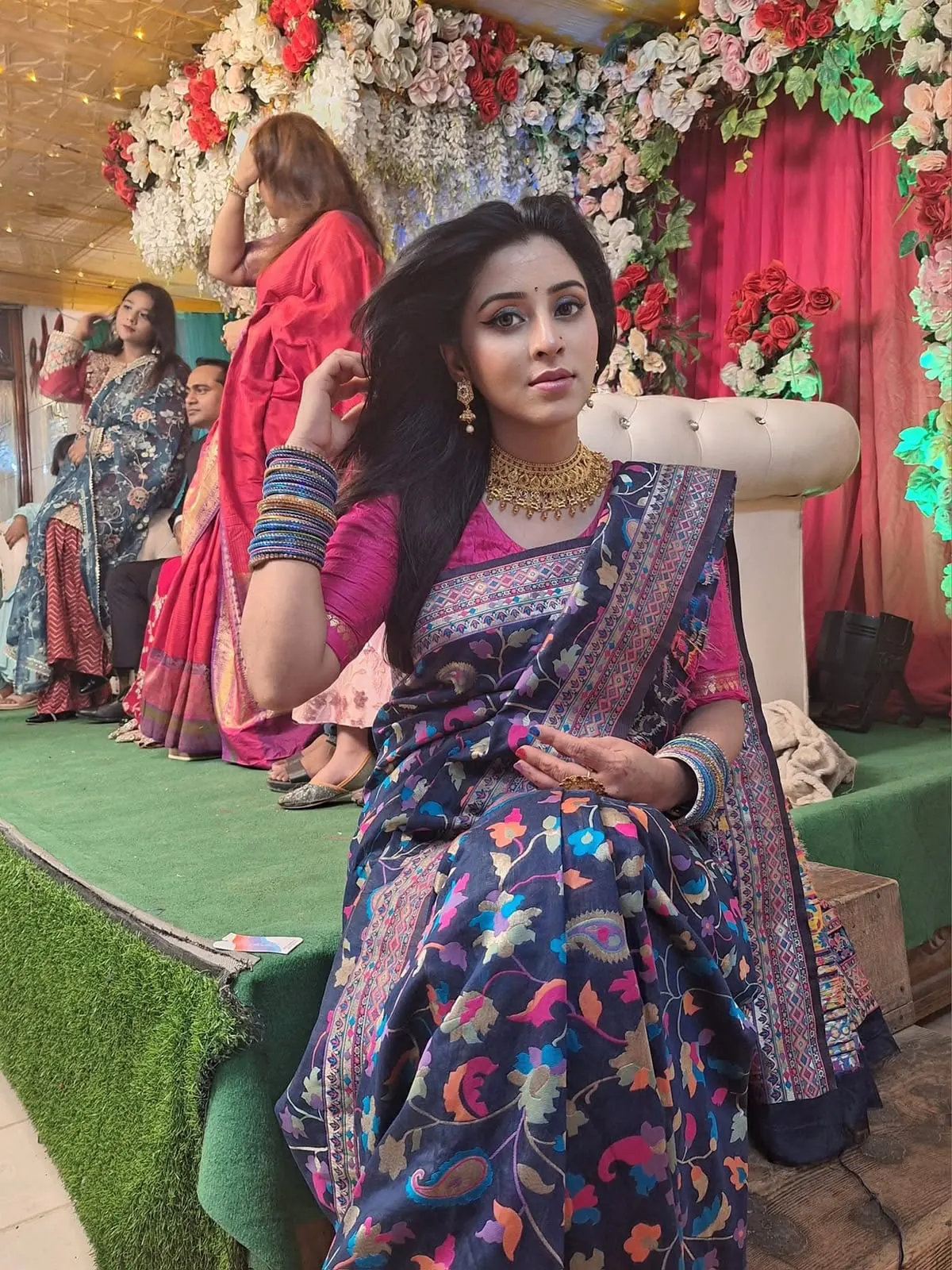 Sumona in a dark floral saree on a decorated event stage