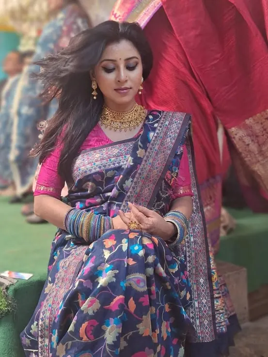 Sumona in a floral saree and gold jewellery looking down