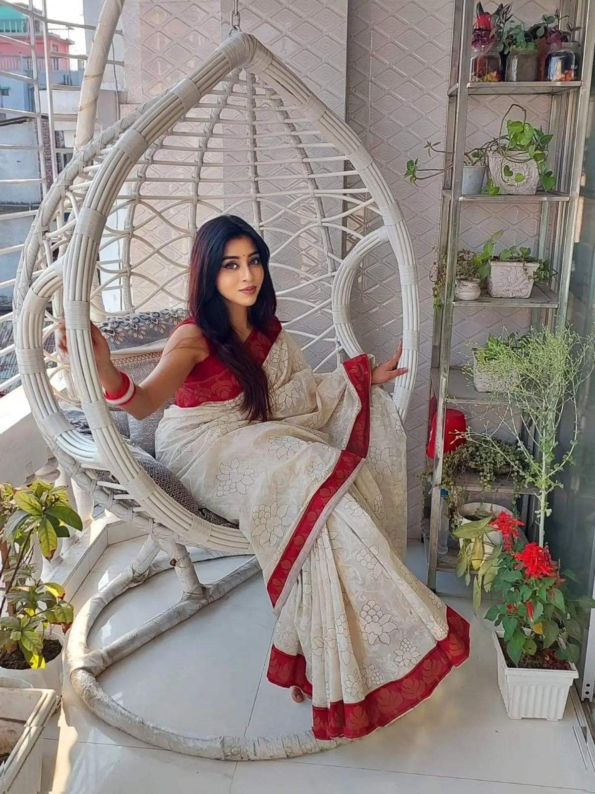 Sumona in a white and red saree seated in a hanging chair