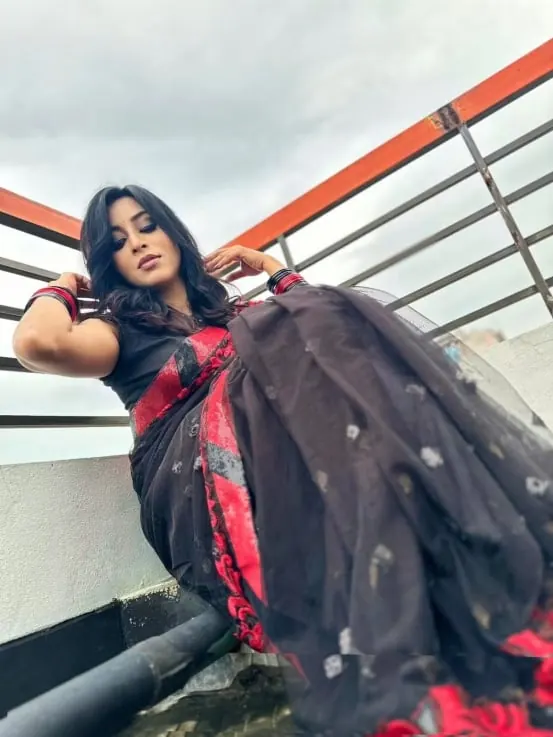 Sumona posing on a rooftop balcony in a black and red saree